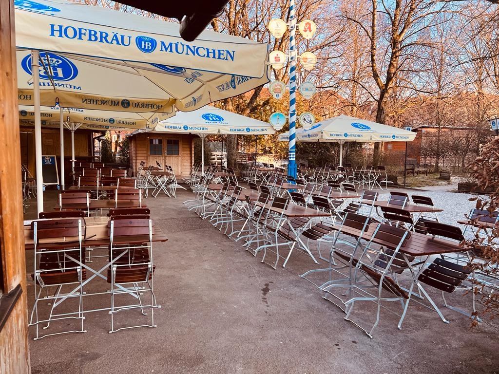 Terrasse mit vielen Tischen, Stühlen und großen Schirmen mit der Aufschrift Hofbräu München