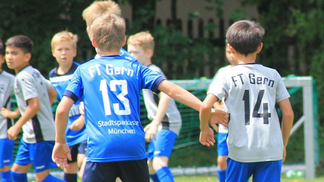 7 Jungs in blauen und grauen Trikots spielen Fussball